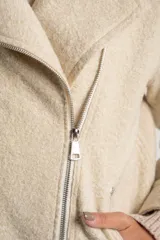 Campera de abrigo color crema, con cuello solapa y cierre asimétrico frontal. Presenta textura bouclé o de lana rizada.