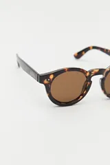 Lentes de sol con marco redondeado de color negro y cristales oscuros. Presentan un diseño clásico con detalles metálicos sutiles en las esquinas del frente.