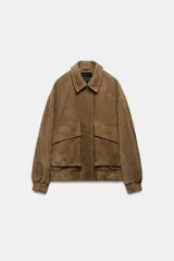 Chaqueta oversize confeccionada en piel de ante, con cuello solapa, manga larga con puños elásticos y bajo elástico. Presenta bolsillos de plastrón con solapa en el frente y cierre frontal con cremallera y botones ocultos.