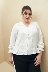 Camisa negra de manga larga con escote en V y botones forrados al tono en el frente. Destaca por su textura sutil y por el detalle de frunces con volados en la parte inferior.