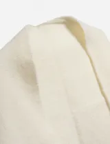 Capa o chal triangular de tejido grueso, color blanco roto o crema, con bordes deshilachados o con flecos.