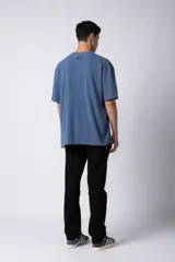 Remera de corte oversized en color marrón, confeccionada en tejido de algodón con textura de micropanal. Presenta cuello redondo con detalle de costura en forma de X y mangas cortas de estilo caído.