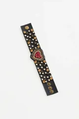 Pulsera de cuero sintético negro con un diseño central de corazón bordado en strass rojos y plateados. La banda está adornada con piedras de cristal en tonos ámbar y transparentes, junto con tachas metálicas en forma de estrella. Posee un cierre ajustable con botones a presión.
