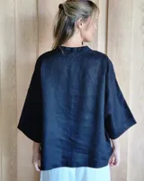 Camisaco de lino negro con cuello en V, cierre frontal con un único botón grande y mangas tres cuartos anchas.