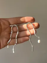 Aros colgantes de alpaca color plateado con forma irregular y perla de río colgante.