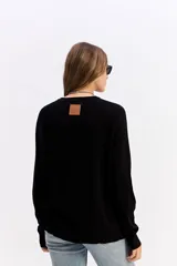 Sweater de punto negro con cuello redondo, manga larga y calce relajado. Presenta una costura vertical central en el frente y puños acanalados.