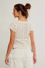 Remera de encaje calado color blanco, con calce ajustado, escote redondo amplio, botonadura corta en el frente y mangas cortas.