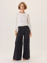 Pantalón de pierna ancha color azul oscuro o negro, con pespuntes a contratono y una tira de contraste en el lateral que estiliza la pierna.