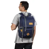 Mochila Jansport modelo Hatchet, color azul marino con detalles en gris y cuero sintético marrón. Presenta un compartimento principal con cierre de cordón y tapa superior con correas ajustables. Incluye bolsillos frontales con tapa y bolsillos laterales para botellas.