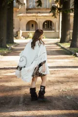 Poncho de lana merino color crudo con cuello alto, diseño amplio y flecos en el ruedo. Presenta bordados decorativos en tono chocolate y detalles de flecos en los hombros.