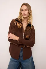 Sobrecamisa de gamuza color marrón con apliques de cuero metalizado en tono cobre en los hombros y bolsillo frontal. Presenta detalles bordados en las mangas, el bolsillo y la espalda, con un diseño de corte recto y cuello camisero.