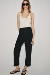 Pantalón de tiro medio con cintura con trabillas, detalle de raya planchada y bajo con aberturas laterales. Cierre frontal con cremallera, botón y ganchos metálicos.