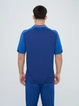 Remera polo deportiva Umbro del Club Nacional de Football, color azul con cuello en V y detalles en rojo y blanco. Incluye el logo de Umbro y el escudo del club.