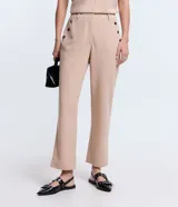 Pantalón slim color beige, confeccionado en crepé, con cierre delantero en la cintura y detalles de ojales en los bolsillos.