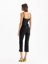 Pantalón negro de tiro alto y calce ajustado, con recortes centrales y tajos en los laterales del ruedo decorados con pequeños moños satinados.