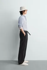 Camisa de algodón de corte relajado, con cuello solapa abotonado (button-down) y manga larga terminada en puño con botón. Presenta un patrón de rayas verticales finas en tonos azul claro y blanco.