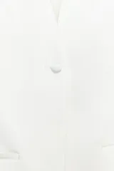 Chaleco de smoking color blanco, con escote en pico, manga sisa y cierre frontal con un botón. Cuenta con falsos bolsillos de vivo en el delantero y forro interior combinado a tono.
