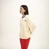 Buzo de algodón color crema, de corte holgado, con cuello redondo ribeteado en azul y logo bordado en el pecho.
