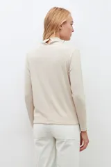 Blusa beige claro con cuello alto y mangas largas, con pequeños brillos.