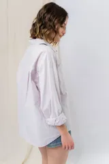 Camisa verde pastel de algodón, corte oversize, con cuello camisero, cierre con botones, mangas largas con puños con volados de encaje blanco, dos bolsillos frontales con solapa y ruedo irregular. 