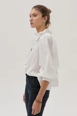 Blusa blanca con lunares en relieve, cuello con volados y lazos, mangas abullonadas 3/4 y bordados con lentejuelas en el frente.