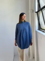 Poncho de tejido de punto color azul jean, con cuello alto y diseño de trenzas verticales. Presenta mangas integradas con puños acanalados y corte holgado.
