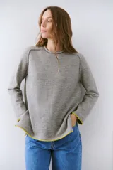 Buzo de tejido de punto color gris melange, con corte relajado y cuello redondo. Presenta costuras visibles en los hombros y detalles de terminación en color amarillo vibrante en los puños y el ruedo.