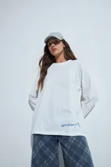 Remera de manga larga en color blanco, con corte relajado y cuello redondo. Presenta un pequeño estampado gráfico en la parte inferior frontal con la frase 'WHO WH WHO?' y un dibujo de un perro.