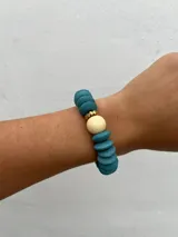 Set de tres pulseras elásticas con cuentas de madera en colores celeste, negro y rosa, con detalles de cuentas doradas y cuentas color crema.