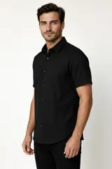 Camisa negra de manga corta, con cuello clásico, cierre frontal con botones y bolsillo ojal en el pecho.