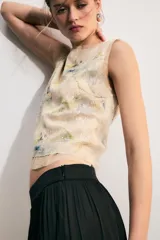 Top corto sin mangas, con cuello redondo, confeccionado en tejido de punto cubierto de lentejuelas con estampado floral en tonos azules y verdes sobre fondo beige. Cuenta con cierre en la espalda con abertura y botón.