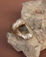 Anillo plateado con forma orgánica irregular y un agujero en el centro.