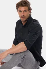 Camisa lisa negra de manga larga con bolsillo en el pecho y presilla para sujetar las mangas enrolladas.