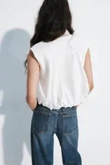 Top blanco de popelín sin mangas, con cuello camisero, corte cropped y cierre frontal con botones.