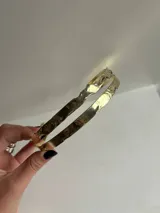 Gargantilla rígida de diseño abierto, confeccionada artesanalmente en bronce con acabado dorado y textura irregular.