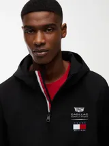 Cortavientos negro con capucha fija, cierre frontal de cremallera con cinta distintiva y puños elásticos. Presenta logos de la colaboración Cadillac Formula 1 Team en el pecho y diseño de corte regular.