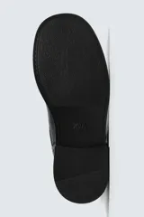 Bota de media caña en color negro, con diseño de horma cuadrada y suela con ligero tacón. Presenta dos cintas ajustables con hebillas metálicas, una en la parte superior de la caña y otra en la zona del empeine.