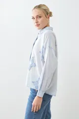 Camisa de corte recto y manga larga en color celeste claro, con diseño de estrellas bordadas en relieve en tono azul. Presenta cuello clásico y cierre frontal con botones.