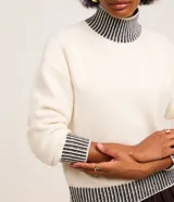 Suéter de punto pesado color blanco con cuello alto, puños y ruedo acanalados en contraste con rayas negras. Presenta diseño de hombros caídos y manga larga.