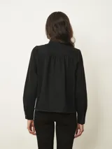 Camisa de jean de corte recto con cuello alto tipo mao con volados, cierre frontal con botones a presión y mangas largas con hombros ligeramente abullonados.