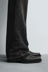 Bota estilo cowboy de caña media, confeccionada en piel negra con costuras decorativas en la caña y el empeine. Presenta una horma en punta, tacón ancho y tiradores laterales.