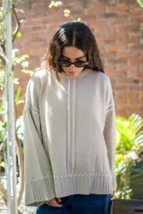Sweater oversize de tejido de punto color beige, con cuello a la base y mangas largas acampanadas. Presenta detalles bordados a mano en color blanco en el frente, hombros y ruedo.