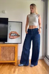 Jean de tiro medio en color azul índigo oscuro, con corte de pierna ancha y costuras verticales decorativas en el frente. Presenta bolsillos delanteros tipo parche y cierre de botón y cremallera.