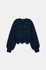 Jersey de punto color azul marino con escote en pico y manga larga. Presenta un diseño texturizado con aplicaciones de flores en relieve del mismo tejido en el cuello y el ruedo.