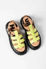 Sandalia tipo gladiadora con plataforma track negra. Presenta un diseño bicolor con tiras delanteras en color amarillo neón y talón con tira ajustable en color beige. Incluye hebilla metálica negra.