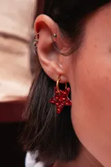 Aro tipo argolla de acero quirúrgico con dije en forma de estrella de color rojo, decorado con cristales brillantes aplicados manualmente.