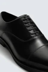 Zapato de vestir tipo oxford con puntera reforzada, confeccionado en piel lisa de color negro. Presenta cierre de cordones, forro interior y plantilla de piel, y suela con tacón bajo.