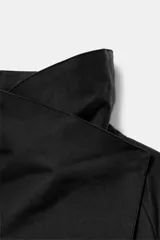 Cazadora corta de color negro con cuello subido cruzado, manga larga con puños anchos ajustados con trabilla y botón, y cierre frontal cruzado con botones ocultos.