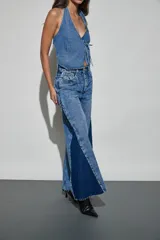 Jean de denim en tonos azul claro y azul oscuro, de tiro alto y corte wide leg, con inserciones laterales en contraste, detalles de tachas metálicas y acabado desmechado en el ruedo.