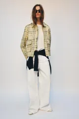 Chaqueta de corte recto confeccionada en tejido con textura de cuadros en tonos amarillos, blancos y negros. Presenta cuello solapa, cierre frontal con botones ocultos, bolsillos de plastrón con solapa en el delantero y mangas largas con puños abotonados.